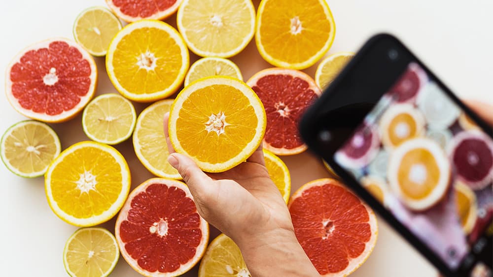 スマートフォンを持ち、さまざまな柑橘類を撮影する女性の手
