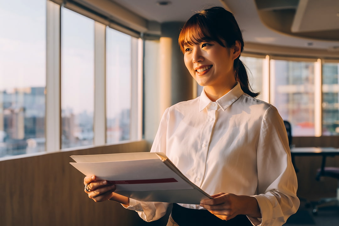 資料を持って夕日を見ながら微笑む女性社員