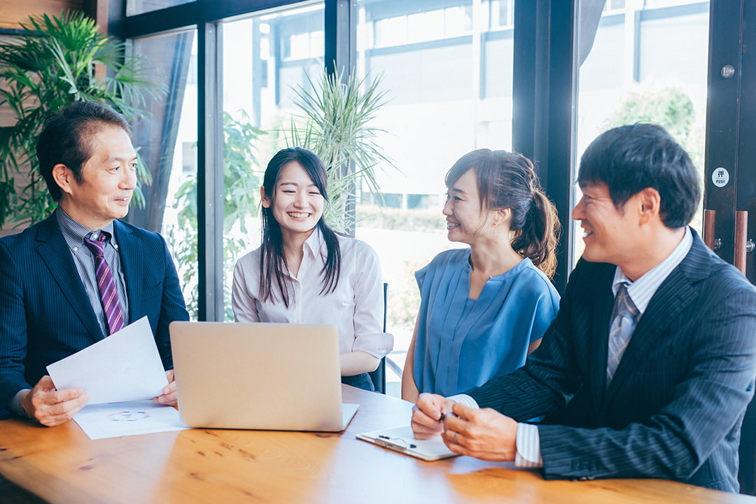 パソコンや資料を持って4人で話をしている男女の社員